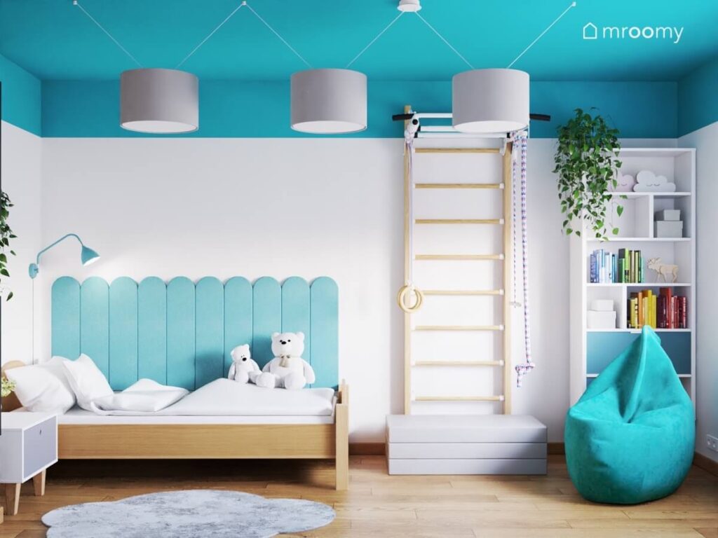 Biało niebieski pokój dla dziewczynki a w nim drewniane łóżko uzupełnione niebieskimi panelami drabinka gimnastyczna regał oraz niebieska pufa a na suficie szare lampy