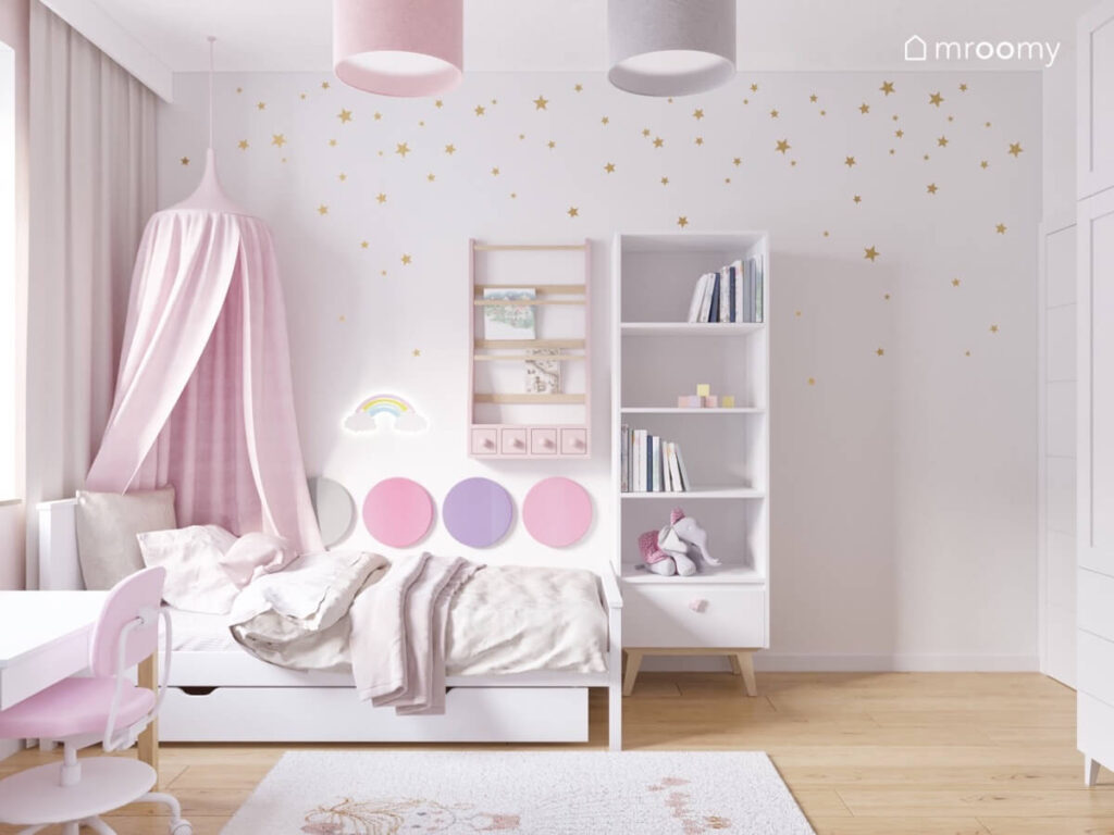 Strefa spania w pokoju dziewczynki a w niej białe łóżko z różowym baldachimem i panelami ściennymi lampka nocna w kształcie tęczy oraz biblioteczka a obok wysoki regał