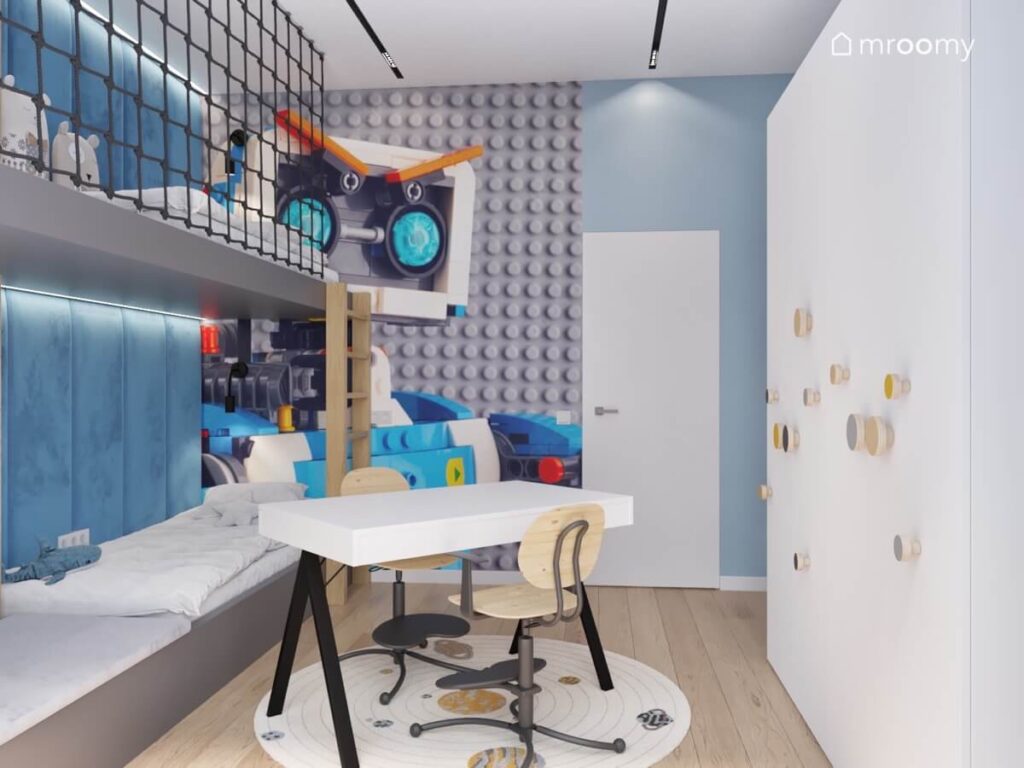 Niebieski pokój dla dwóch chłopców z dużą białą szafą biurkiem na środku oraz tapetą Lego