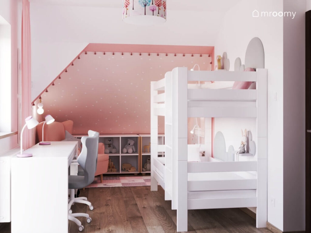Biało różowy poddaszowy pokój dla rodzeństwa z białym łóżkiem piętrowym biurkiem oraz różowym fotelem i niskim regałem pod skosem
