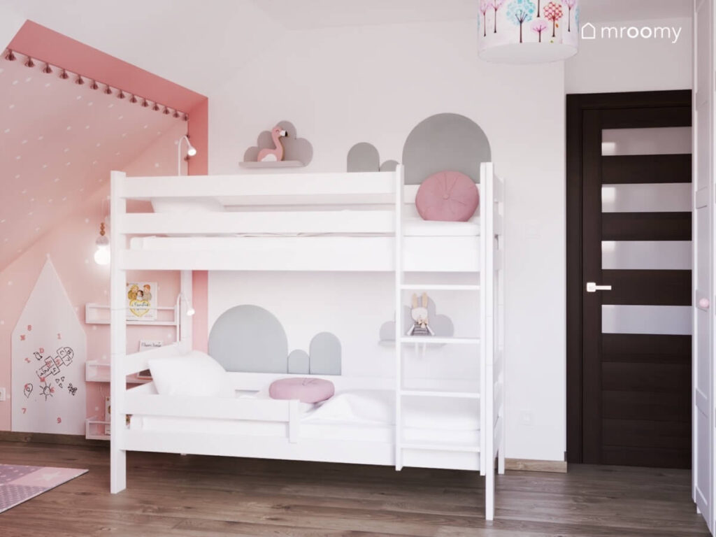 Białe łóżko piętrowe uzupełnione szarymi panelami i półkami chmurki w biało różowym poddaszowym pokoju dla dwóch dziewczynek