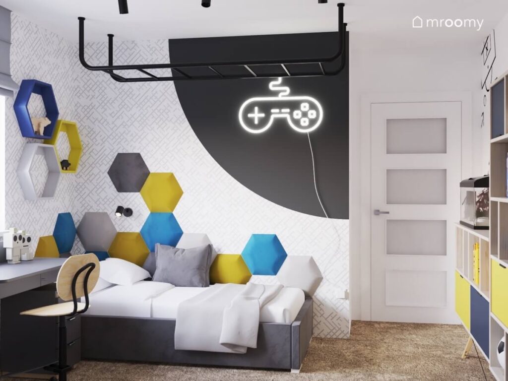 Jasny pokój dla chłopca z szarym tapicerowanym łóżkiem kolorowymi panelami ściennymi oraz ledonem w kształcie pada i drabinką sufitową