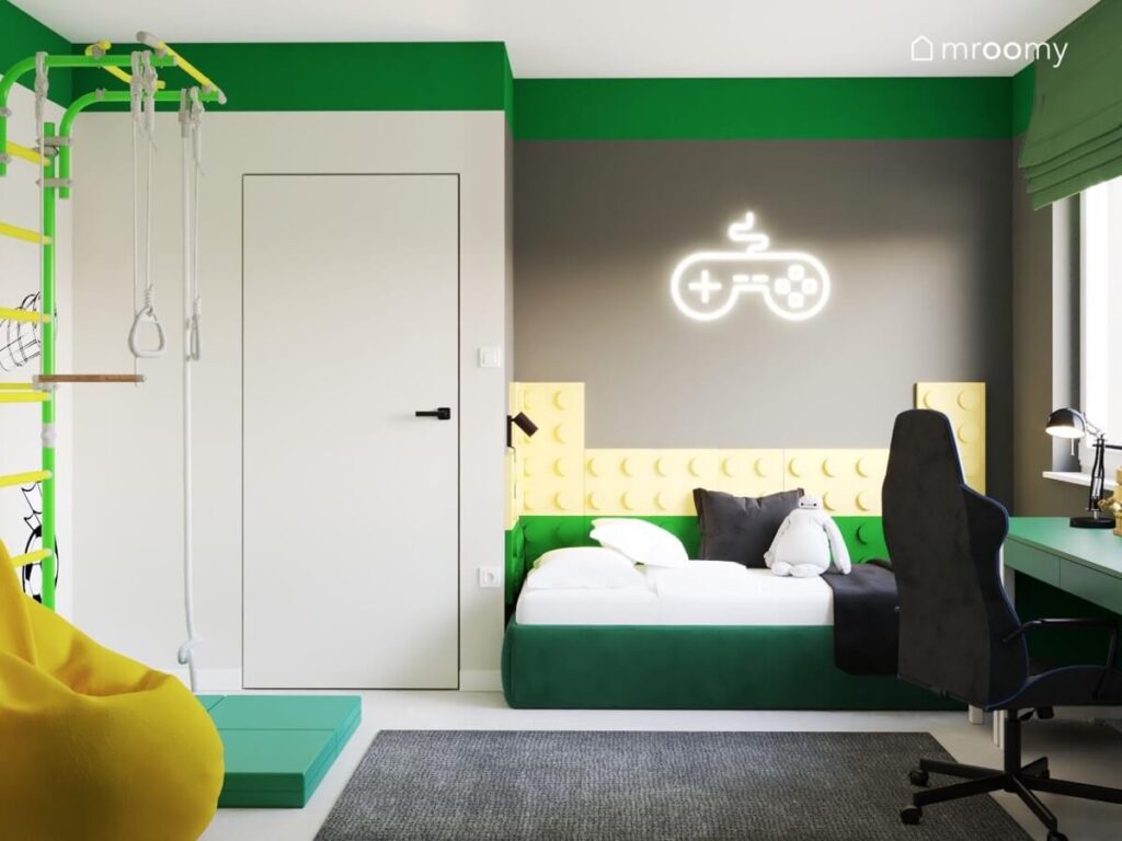 Strefa spania w szaro zielonym pokoju dla chłopca a w niej zielone tapicerowane łóżko uzupełnione panelami w kształcie klocków a nad nim ledon w kształcie pada