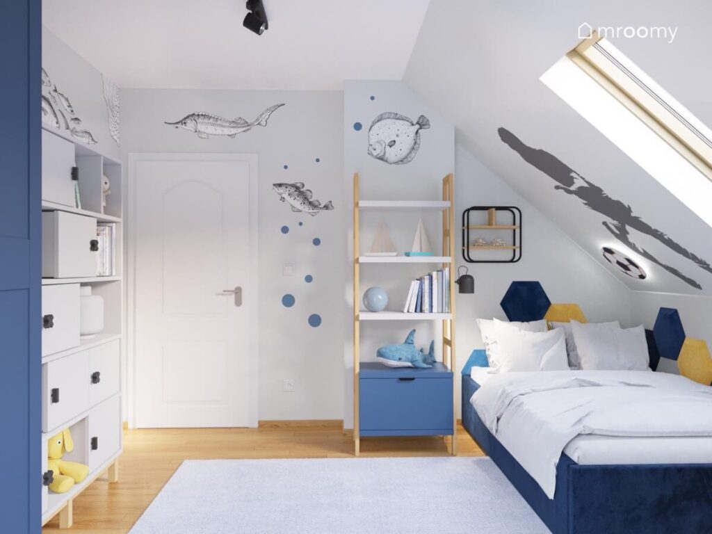 Szaro błękitny pokój dla chłopca z ciemnoniebieskim tapicerowanym łóżkiem regałem drabinką oraz naklejkami ściennymi w kształcie ryb