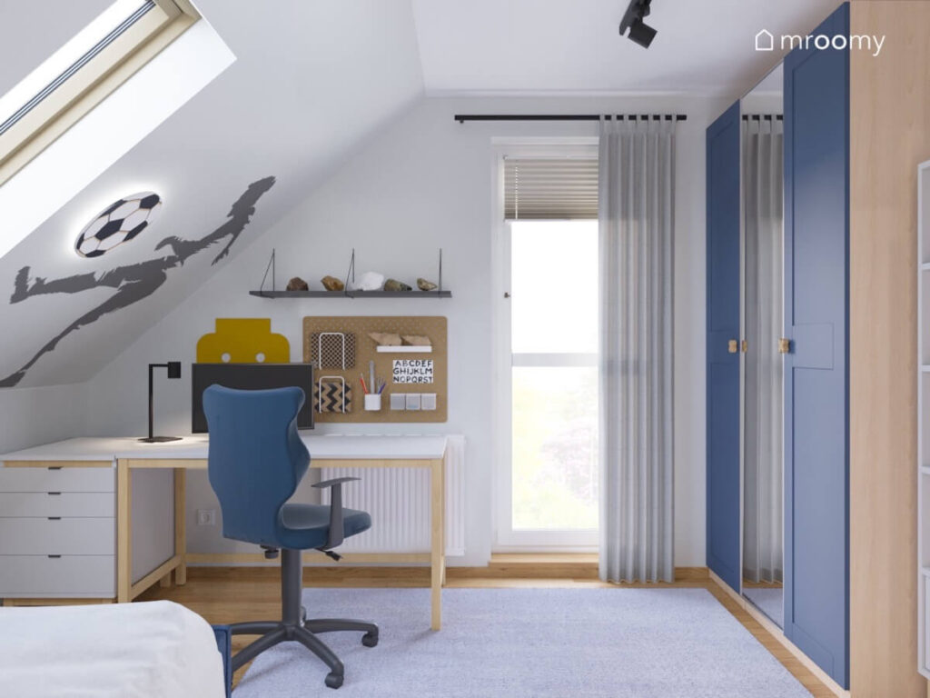 Jasny poddaszowy pokój dla chłopca z niebieską szafą oraz drewnianym biurkiem z białym blatem