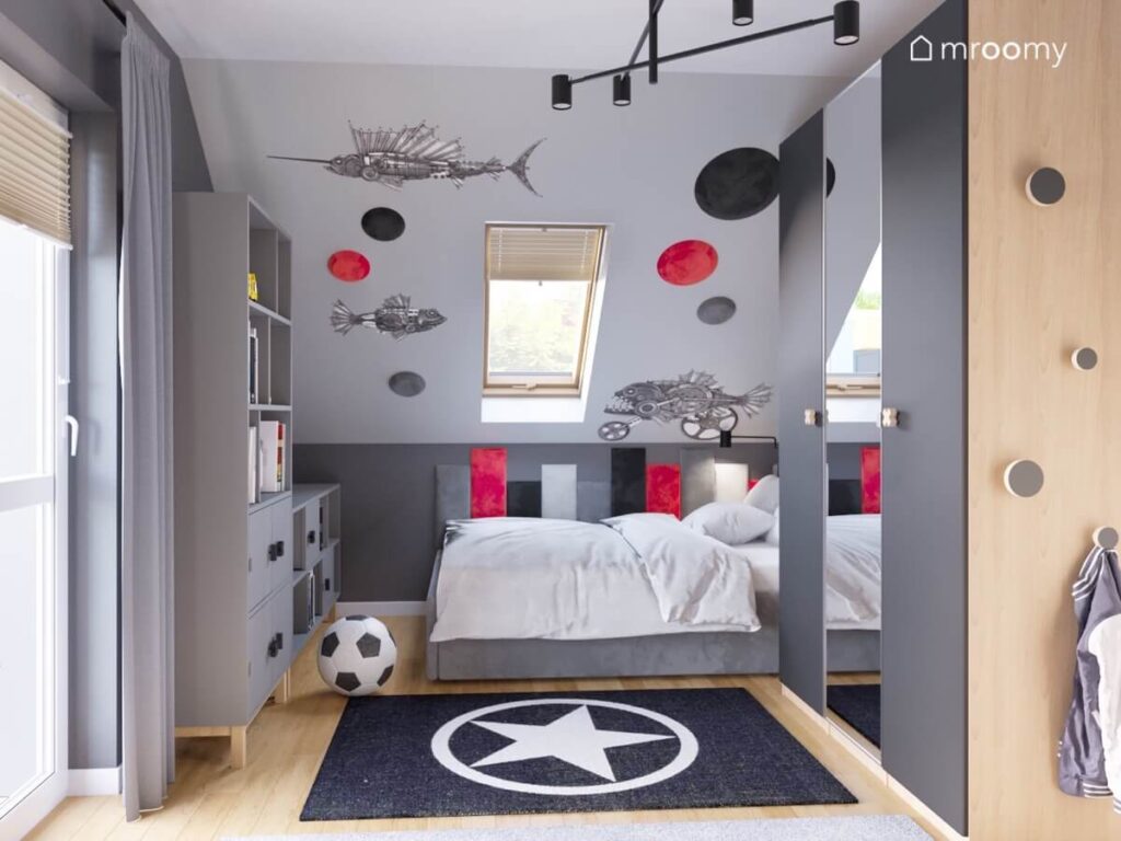 Szare tapicerowane łóżko w pokoju chłopca a nad nim szare czarne i czerwone panele ścienne oraz naklejki mechaniczne ryby