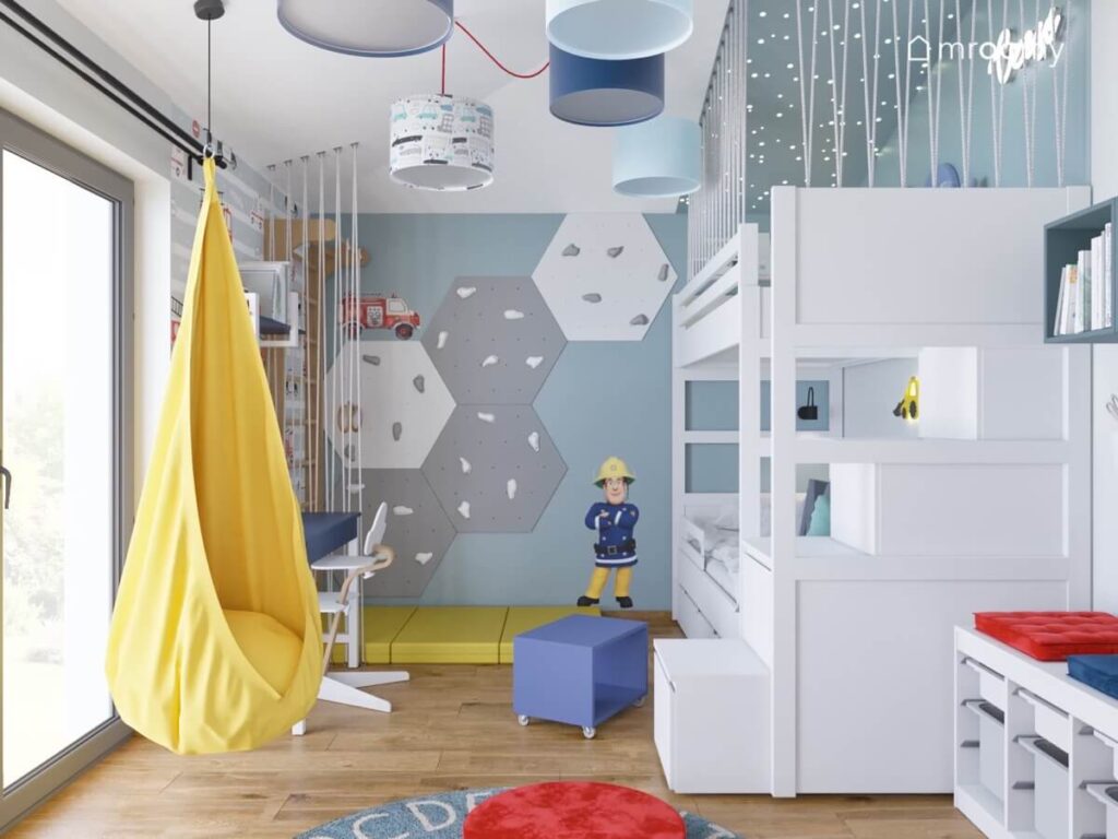 Biało niebieski pokój dla chłopca z białym łóżkiem piętrowym panelami wspinaczkowymi oraz żółtym fotelem kokon