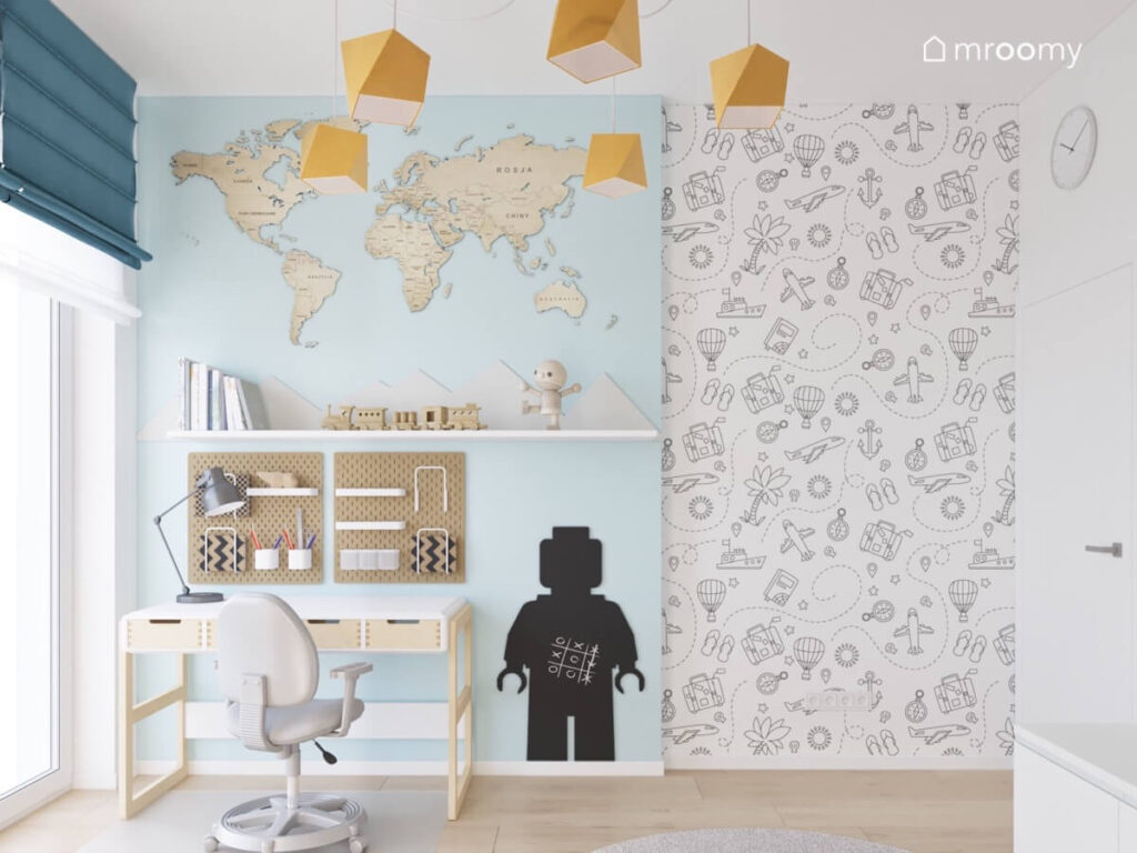 Strefa nauki w pokoju dla chłopca z biurkiem z szufladami organizerami półką oraz mapą świata i tablicą kredową w kształcie ludzika a obok tapeta z motywami podróżniczymi