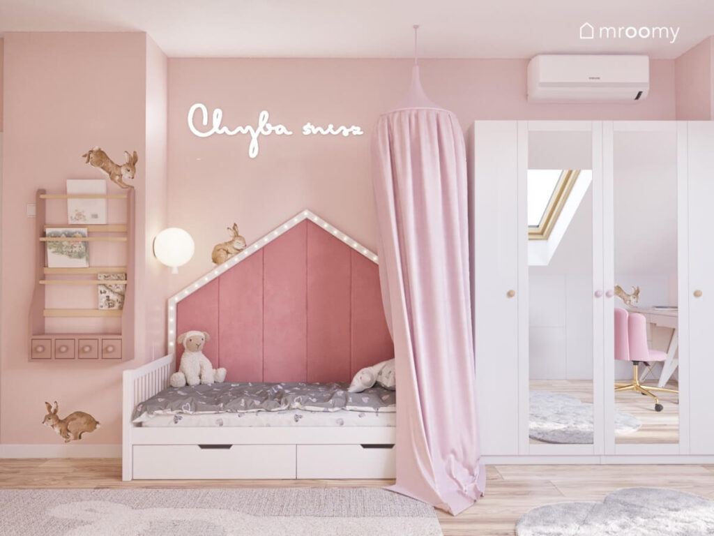 Różowy pokój dla dziewczynki z łóżkiem domkiem z baldachimem biblioteczką oraz szafą z lustrzanymi frontami i królikami na ścianach