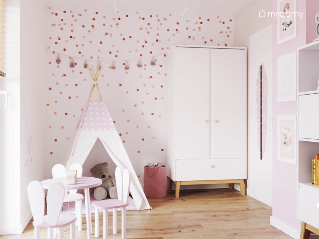 Ściana w pokoju dla dziewczynki pokryta kropkami w różnych odcieniach różu a poza tym namiot tipi i dwudrzwiowa szafa