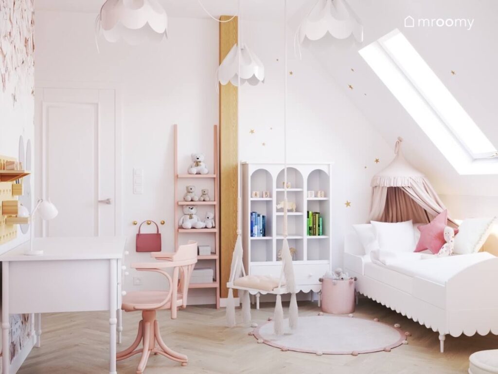 Biały poddaszowy pokój dla dziewczynki ze złotymi gwiazdkami na ścianach różowym regałem drabinką łóżkiem ozdobionym baldachimem i huśtawką wiszącą