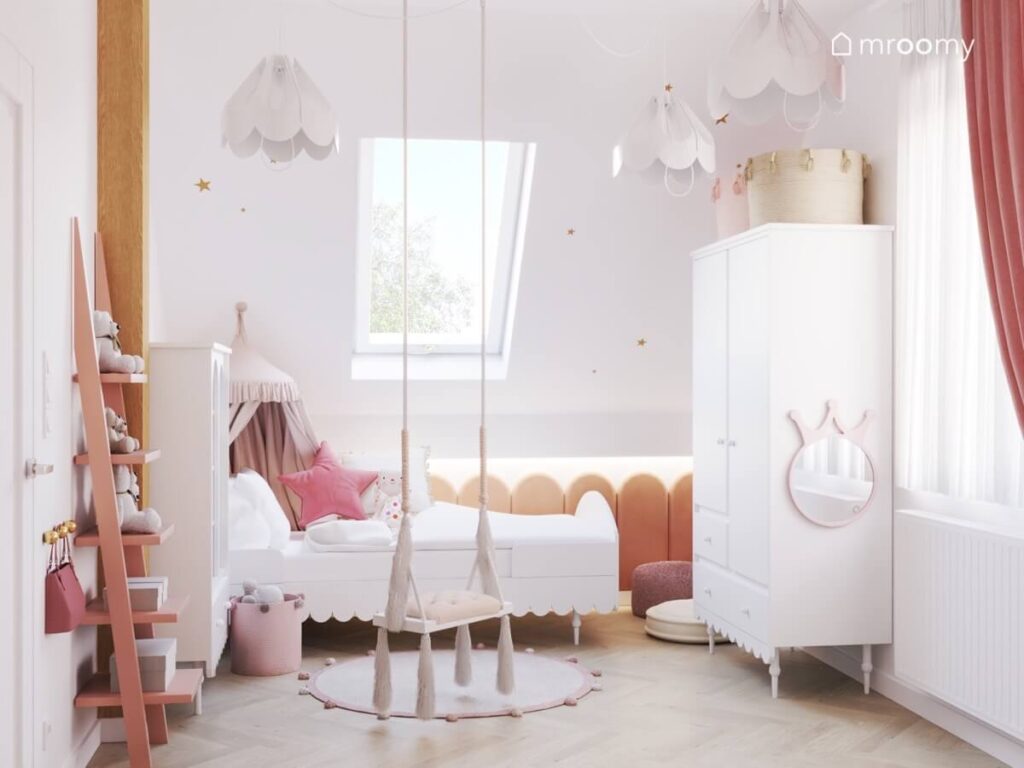 Strefa spania w poddaszowym pokoju kilkuletniej dziewczynki a w niej białe łóżko ozdobione baldachimem a za nim panele ścienne a obok szafa z umocowanym lustrem