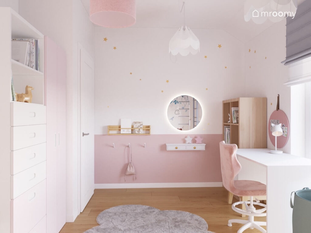 Biało różowa ściana w pokoju dziewczynki a na niej złote gwiazdki lustro oraz półki i uchwyty