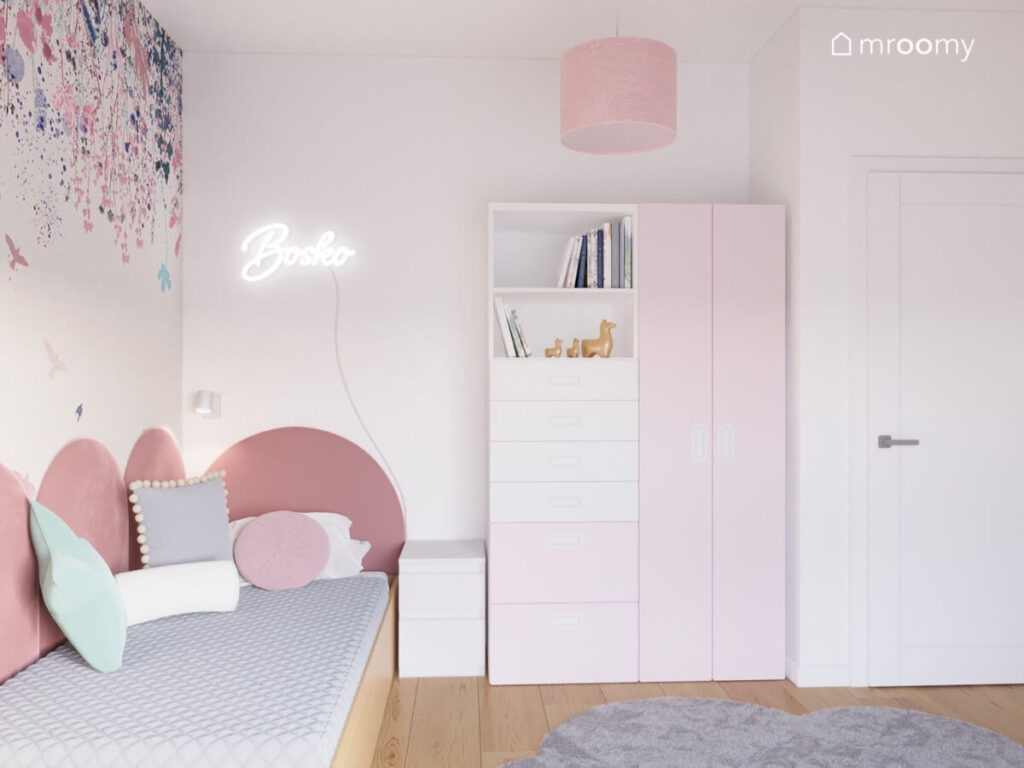 Biały pokój dla dziewczynki z drewnianym łóżkiem uzupełnionym miękkimi panelami ledonem oraz biało różową szafą
