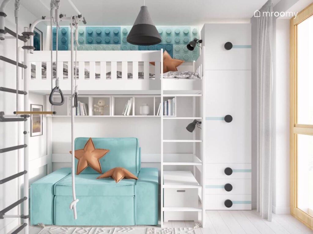 Biała antresola w pokoju dla chłopca a na niej miejsce do spania uzupełnione niebieskimi panelami w kształcie klocków a pod spodem błękitna kanapa