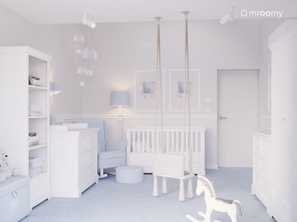 Kącik spania w pokoju dla malutkiego chłopca a w nim białe łóżeczko niebieskofioletowy fotel a na ścianie plakaty z misiami i wiszące balony