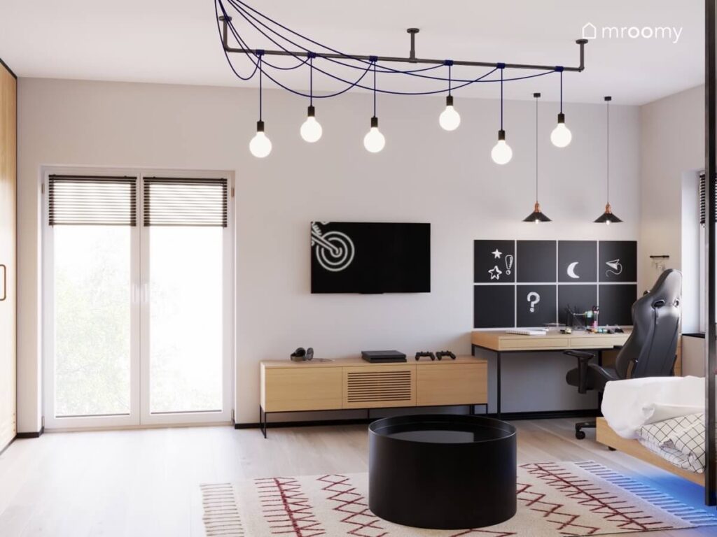 Szary pokój dla chłopca z drewnianym biurkiem i szafką rtv telewizorem oraz kilkoma tablicami kredowymi oraz oryginalnym oświetleniem sufitowym