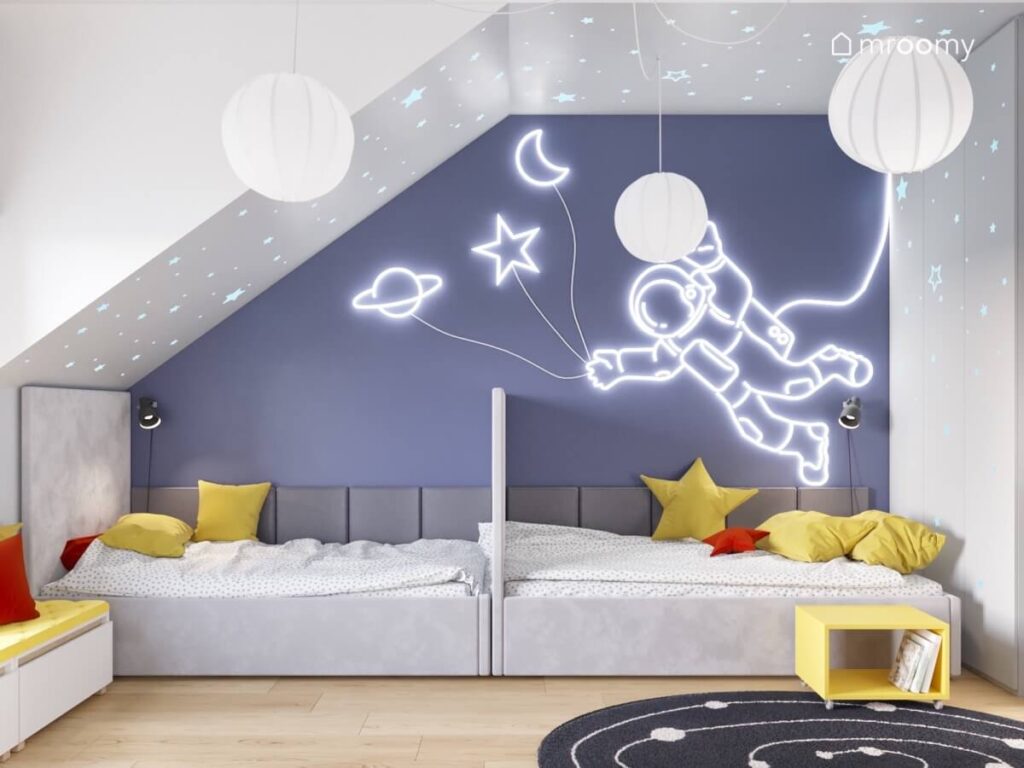 Kosmiczna strefa spania w pokoju dwóch chłopców a w niej szare tapicerowane łóżka na ścianie ledon w astronautą a u sufitu papierowe lampy