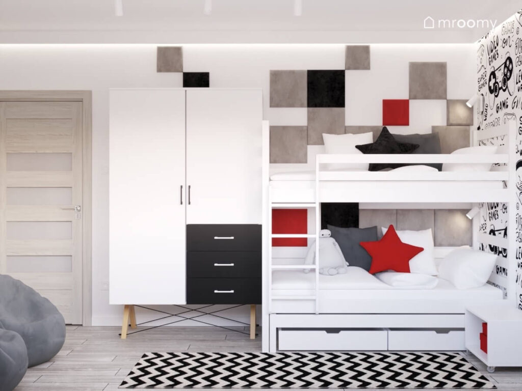 Strefa spania w pokoju dla rodzeństwa a w niej łóżko piętrowe uzupełnione kwadratowymi panelami w różnych kolorach a obok biała szafa z czarnymi szufladami a na podłodze biało czarny dywan