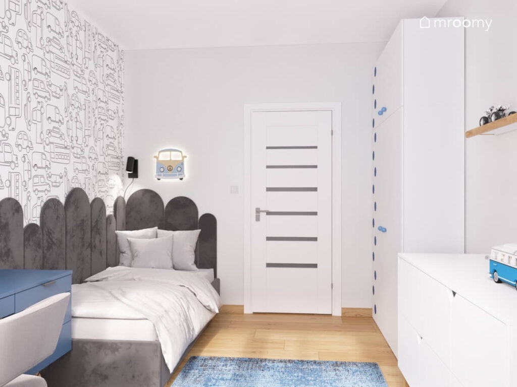 Jasnoszary pokój dla chłopca z tapetą w samochody ciemnoszarym tapicerowanym łóżkiem i białymi meblami