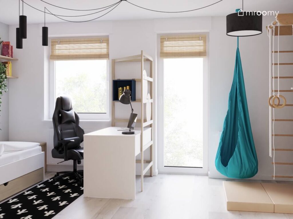 Jasny pokój dla chłopca w wieku szkolnym a w nim białe biurko z ergonomicznym fotelem niebieski fotel kokon dywan w kaktusy oraz czarne lampy