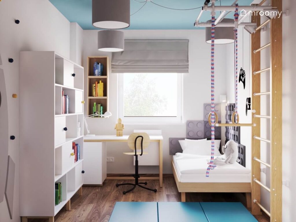 Biały pokój dla chłopca z niebieskim sufitem biało drewnianymi meblami drabinką gimnastyczną i niebieskimi materacami