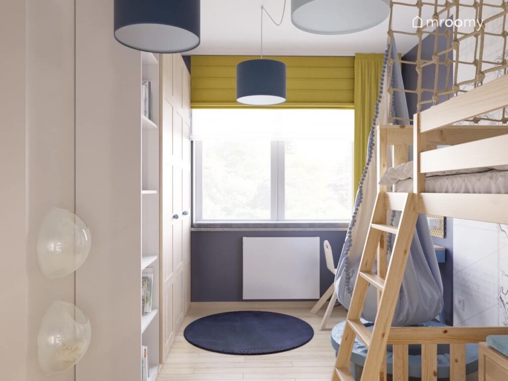 Drewniana antresola jasnoniebieski fotel kokon i jasna szafa a także żółte rolety i zasłony oraz granatowy dywan i lampy sufitowe w pokoju dla chłopca