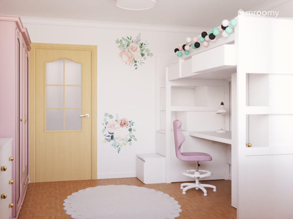 Biała antresola z girlandą cotton balls i strefą nauki pod spodem a na ścianie naklejki kwiaty w pokoju dziewczynki