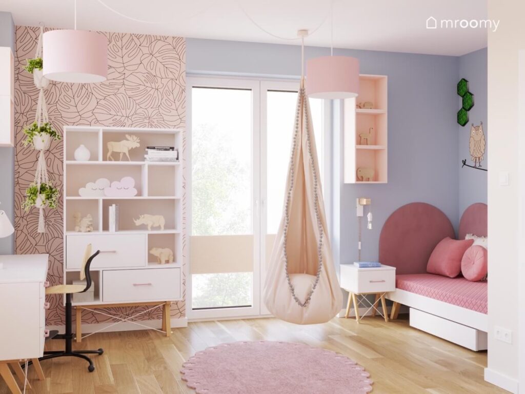 Fragment ściany pokryty tapetą w liście a na niej regał obok fotel kokon oraz łóżko na tle fioletowej ściany w pokoju dziewczynki