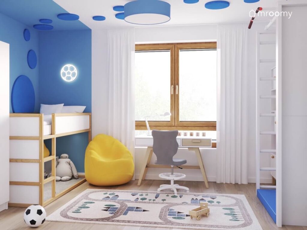 Biało niebieski pokój dla chłopca z biało drewnianymi meblami drabinką gimnastyczną żółtą pufą oraz dywanem miasto