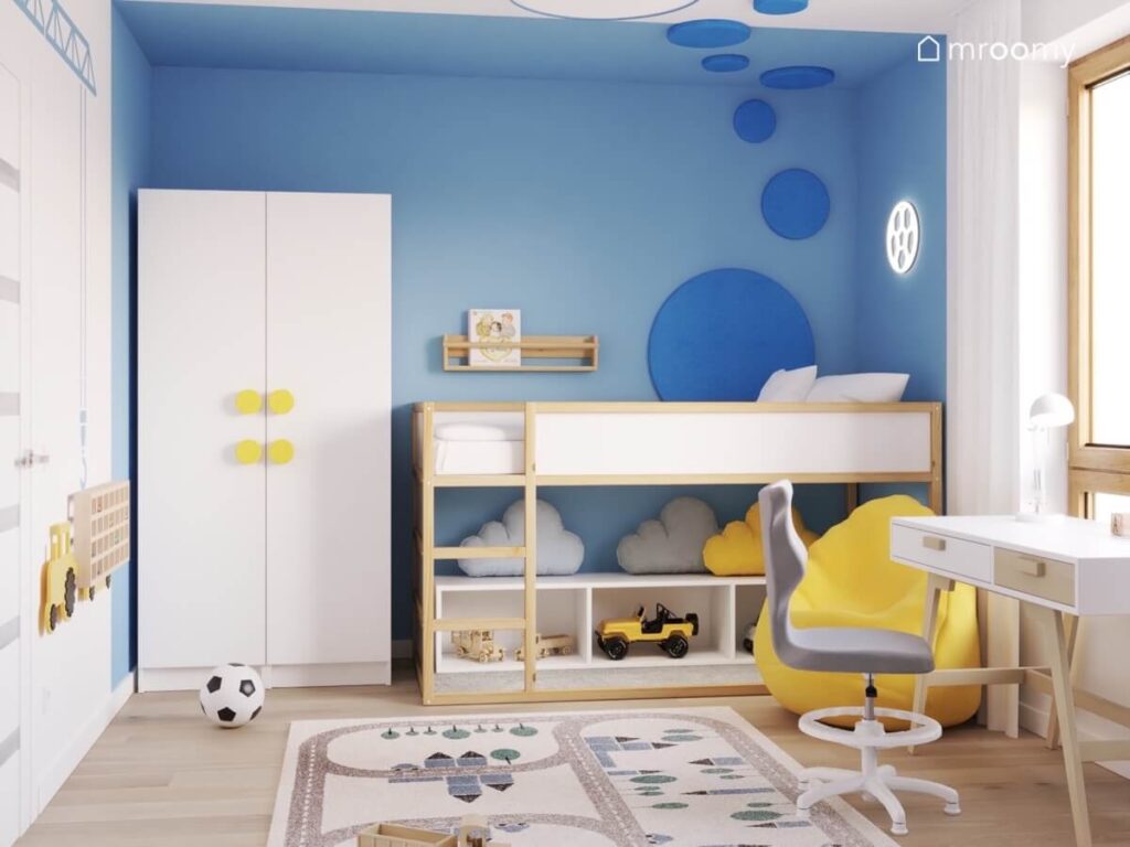 Niebieska strefa spania w pokoju dla chłopca z biało drewnianym łóżkiem ledonem piłka i miękkimi niebieskimi panelami a obok biała szafa