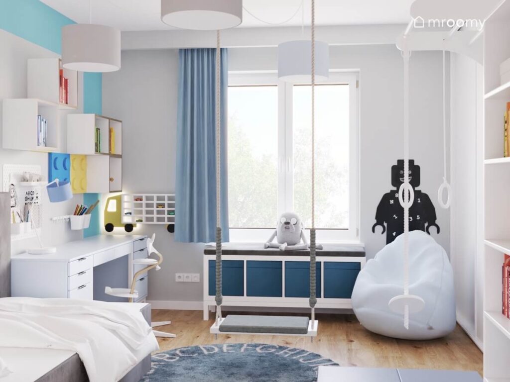 Szaro błękitny pokój dla chłopca a w nim białe meble pufa huśtawka i dywan z alfabetem