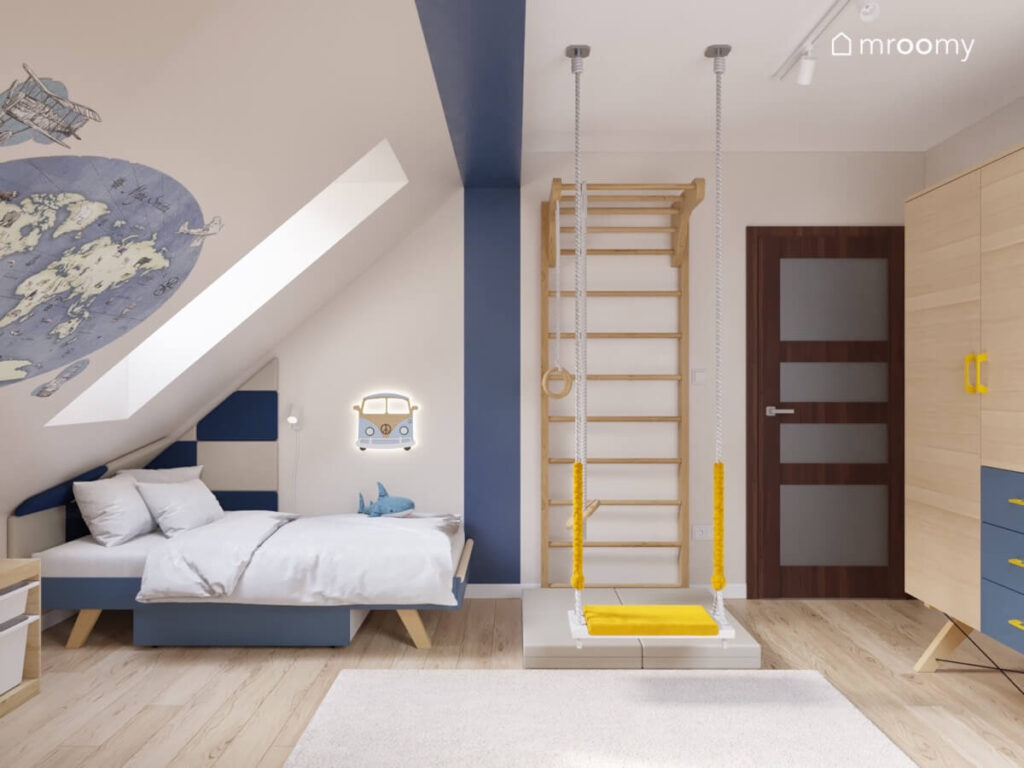 Strefa spania w pokoju dla chłopca a w niej granatowe łóżko panele ścienne mapa świata i lampka van a obok drewniana drabinka gimnastyczna i żółta huśtawka na środku