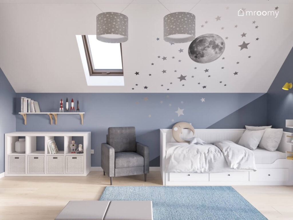 Strefa spania w poddaszowym pokoju chłopca a w niej białe łóżko z szufladami obok szary fotel a na suficie srebrne gwiazdki i księżyc