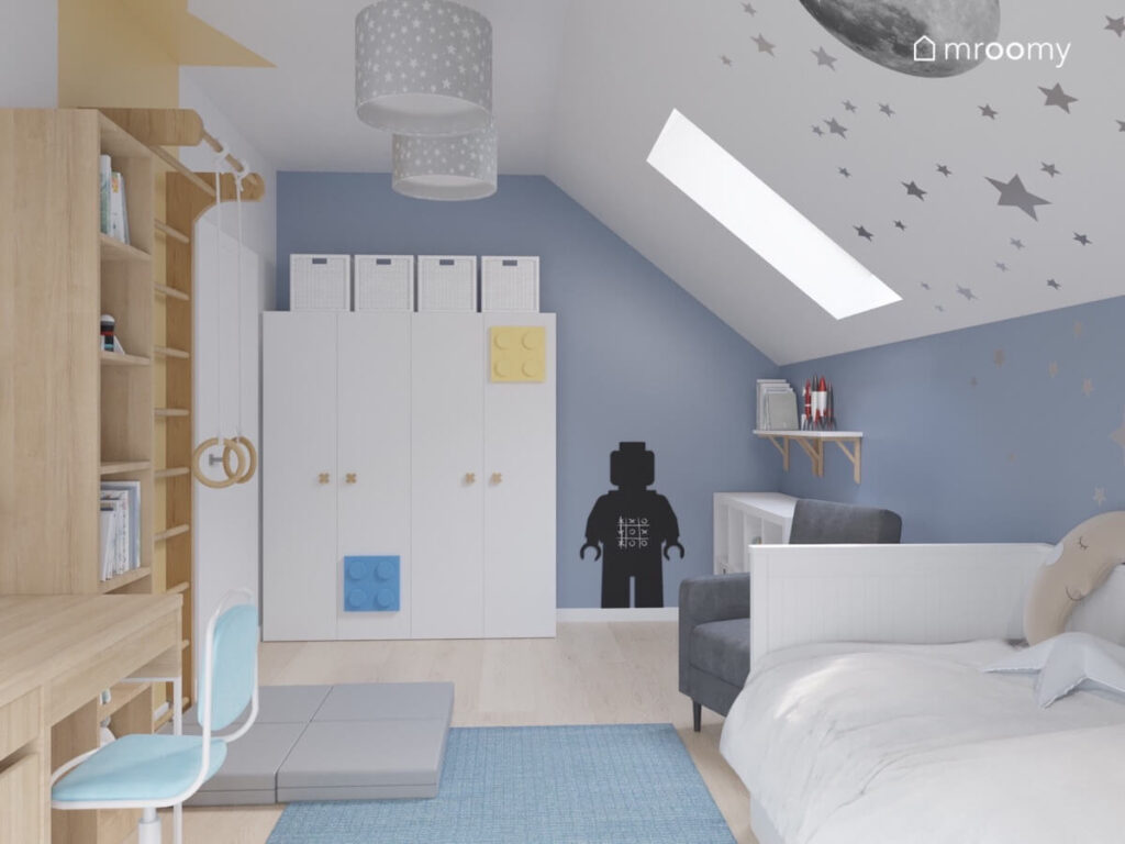 Biało niebieski poddaszowy pokój dla chłopca z białą szafą i łóżkiem a także drewnianą drabinką gimnastyczną i motywami kosmosu