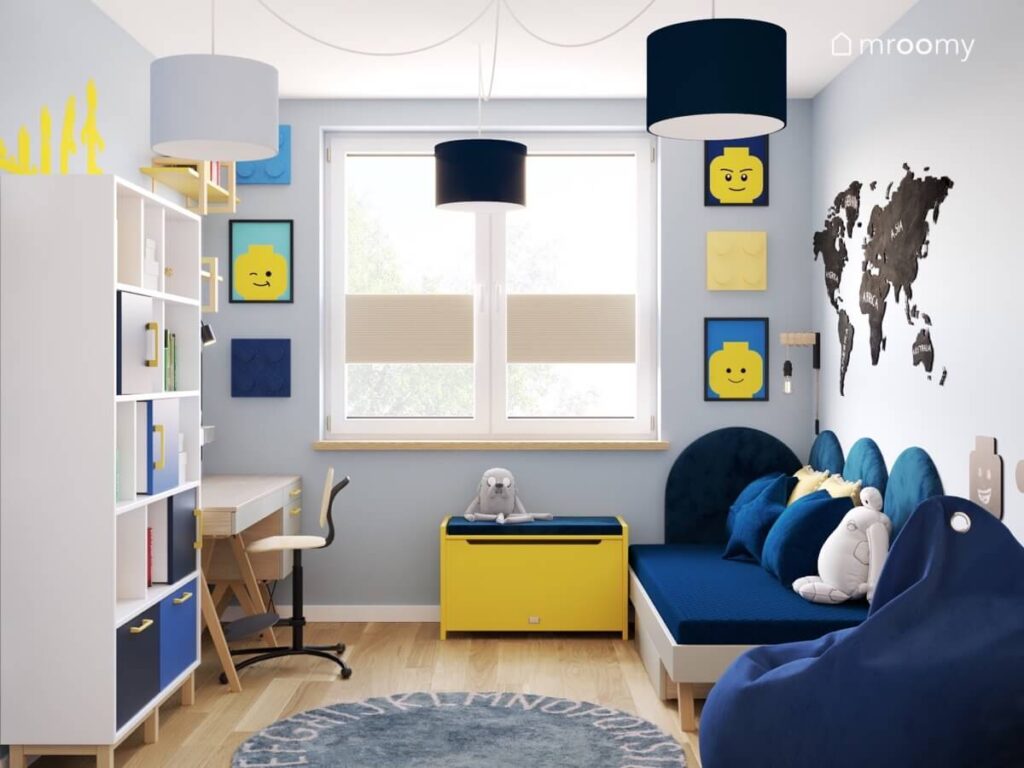 Jasnoniebieski pokój dla chłopca z prostym łóżkiem ciemnoniebieską pufą dywanem z alfabetem oraz obrazki z Lego na ścianie