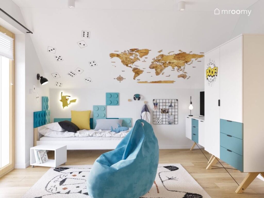 Strefa spania w pokoju dla chłopca uzupełniona miękkimi panelami w kształcie klocków oraz lampką Pikachu a na skosie mapa świata i naklejki kostki