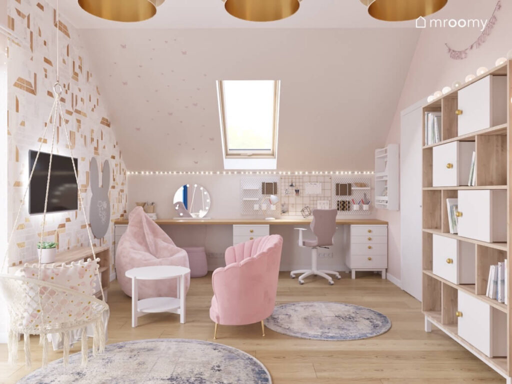 Jasny pokój na poddaszu dla dziewczynki z drewnianym blatem pod skosem stanowiącym biurko oraz toaletkę oraz z różową sofą pufą i małym stolikiem