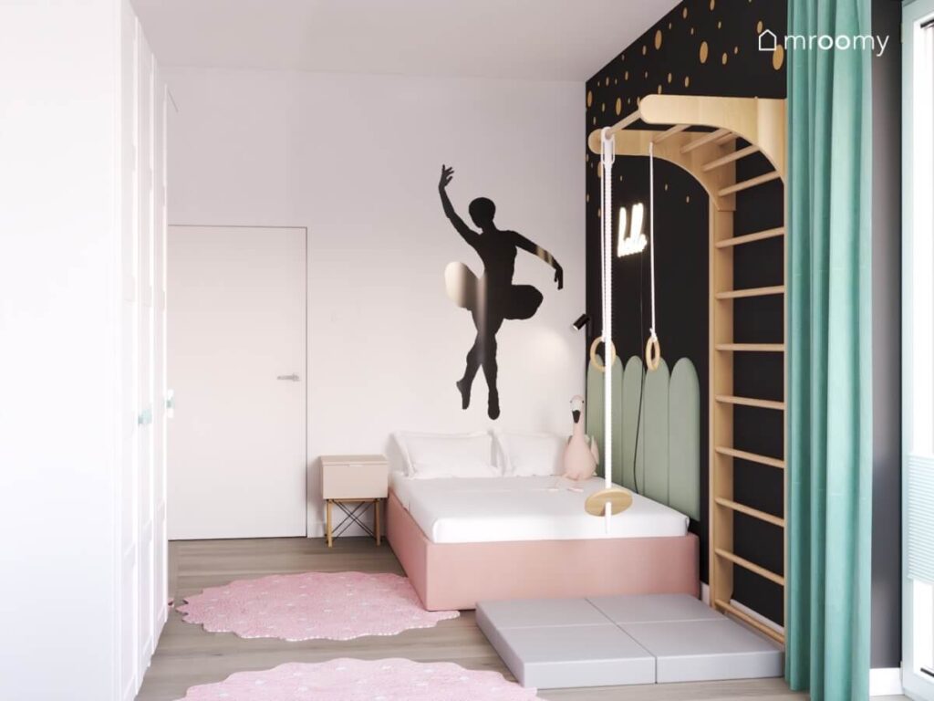 Biało czarny pokój dla dziewczynki z różowym tapicerowanym łóżkiem uzupełnionym zielonymi panelami naklejką ścienną w kształcie baletnicy oraz drabinką gimnastyczną