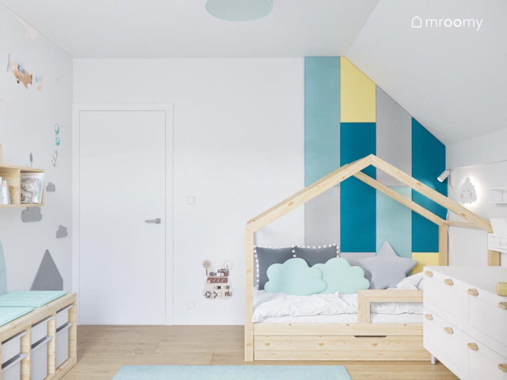Strefa spania w poddaszowym pokoju małego chłopca a w niej drewniane łóżko domek oraz różnokolorowe panele ścienne