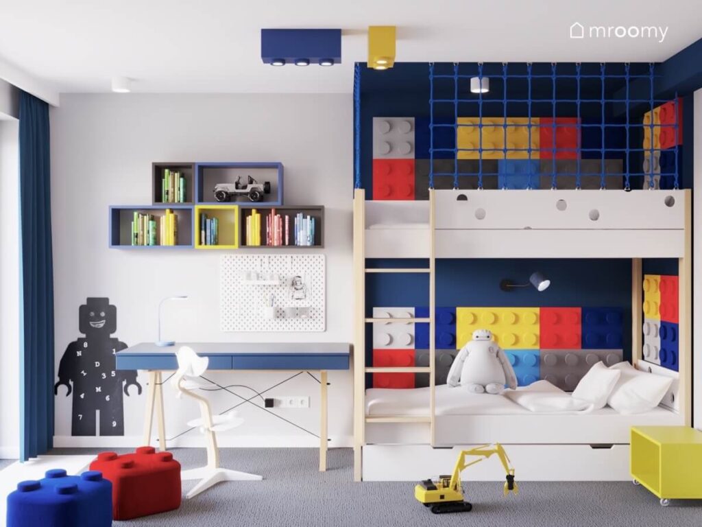 Strefa nauki w pokoju dla chłopca z granatowym biurkiem organizerem półkami i tablicą kredową w kształcie ludzika Lego a obok łóżko piętrowe uzupełnione kolorowymi panelami klocki