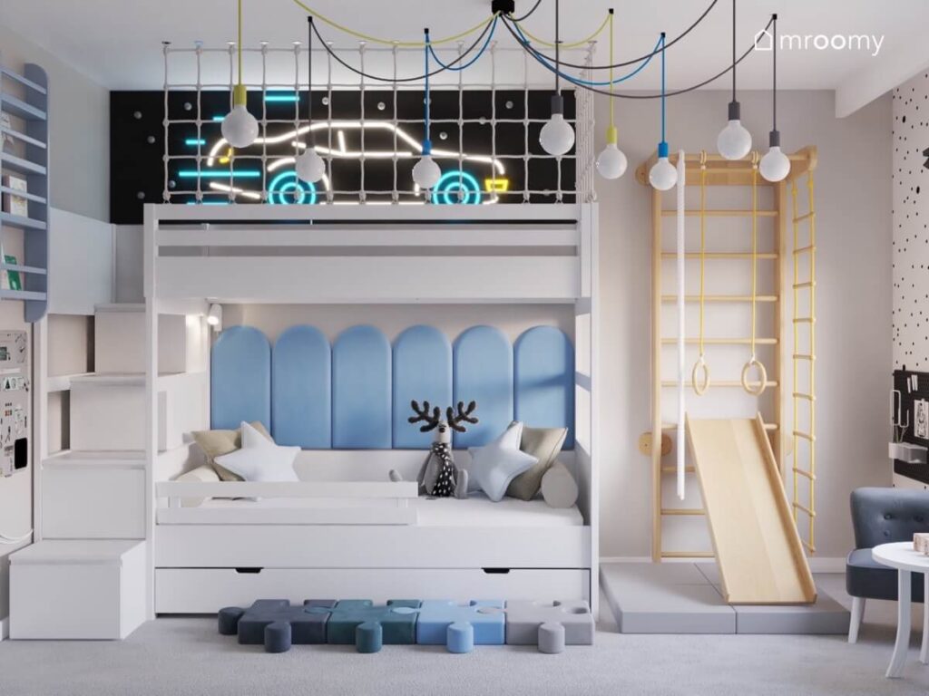 Antresola z miejscem do zabawy oświetlona ledonem w kształcie samochodu pod spodem łóżko z niebieskimi panelami a obok drewniana drabinka gimnastyczna ze zjeżdżalnią w pokoju chłopca