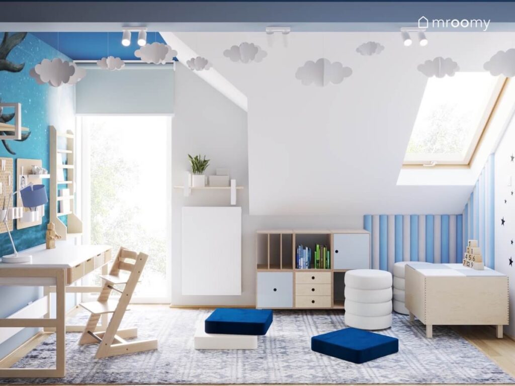 Jasny poddaszowy pokój dla chłopca z biało drewnianymi meblami niskimi pufkami oraz chmurkami u sufitu