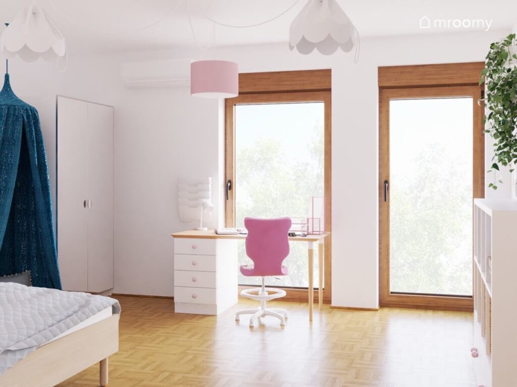 Strefa nauki w pokoju dziewczynki z biało drewnianym biurkiem i różowym krzesłem a na suficie lampy bezy