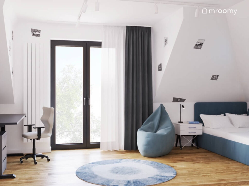 Jasny poddaszowy pokój dla chłopca z granatowym tapicerowanym łóżkiem niebieską pufą i dywanem oraz naklejkami na ścianach