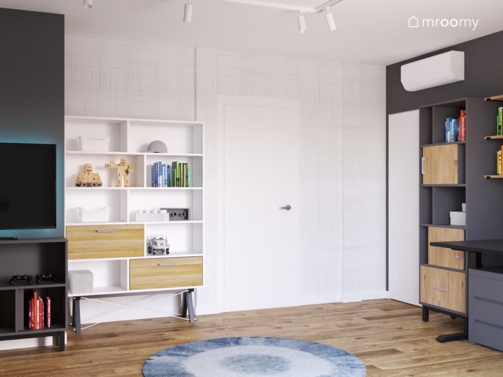 Jasny pokój dla chłopca z białymi i ciemnoszarymi meblami z drewnianymi szufladami minimalistyczną tapetą oraz niebieskim dywanem