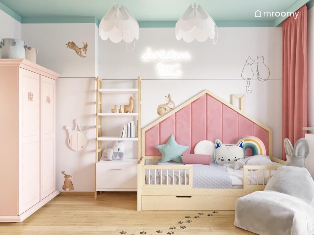 Strefa spania w pokoju dziewczynki z drewnianym łóżkiem domkiem uzupełnionym różowymi panelami oraz ledonem a na ścianie naklejki króliki i koty