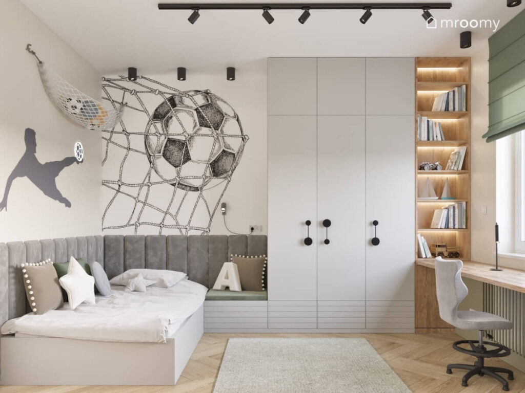 Łóżko uzupełnione szarymi panelami ściennymi duża szafa i drewniany regał a na ścianach piłkarskie naklejki w pokoju dla chłopca