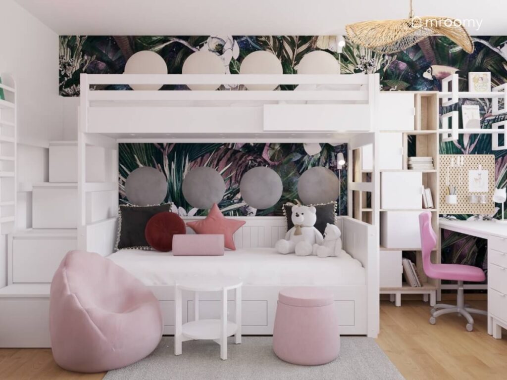 Na pierwszym planie mały stolik z dwoma różowymi pufami za nimi łóżko piętrowe obok regał a na ścianie za nimi tapeta w dżunglę i okrągłe panele ścienne w pokoju dla dziewczynek