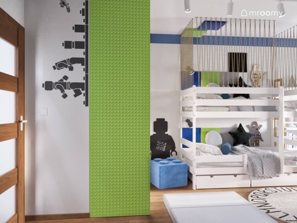 Szara ściana w pokoju dwóch chłopców z naklejką z ludzikiem Lego obok zielona szafa i białe łóżko piętrowe